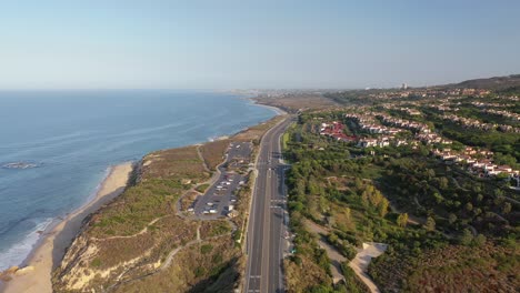 an aerial drone shot gliding down the orange county coastline revealing luxury homes with a view of crashing ocean waves on a stunningly sunny day