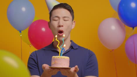 studio portrait of man wearing party hat celebrating birthday blowing out candles on cake with paper confetti 1