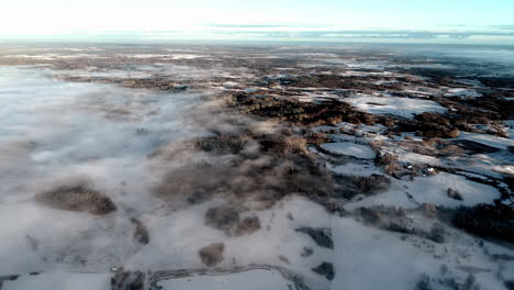 aerial drone flying through clouds over snow-covered landscape with coniferous trees during sunrise