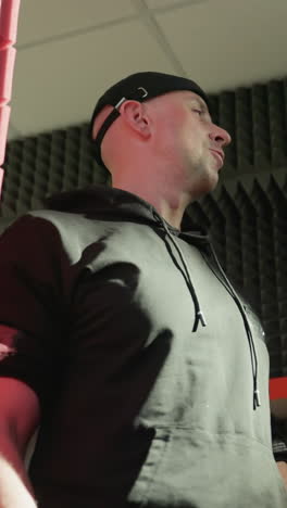 hombre con camisa negra y gorra se involucra con entusiasmo en una conversación en una sala de estudio a prueba de sonido con acentos rojos, con otra persona parcialmente visible