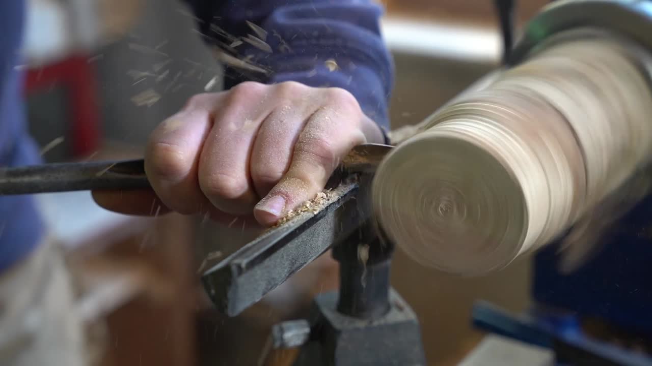 Carpenter woodworker shaving a beam of wood to a round shape with a chisel, Close up shot