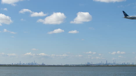 new york city skyline on clear day with passenger jet crossing overhead on approach to landing at jfk airport