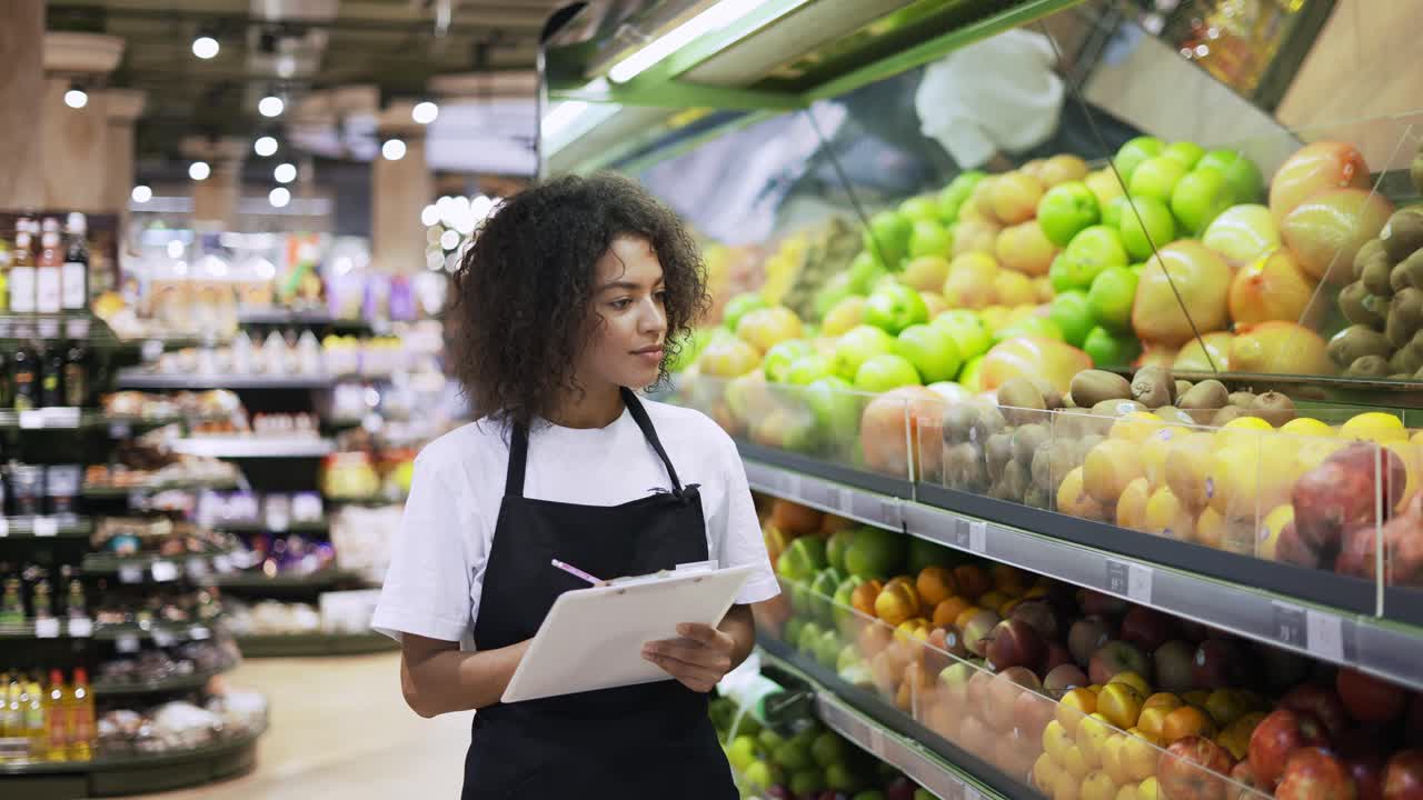 retrato de una mujer afroamericana de pie frente a los estantes de frutas con una tableta