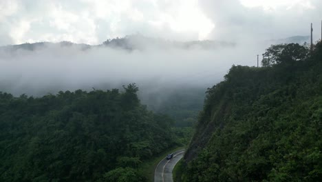 blue suv rounds corner in mountain road dividing valley with epic low clouds