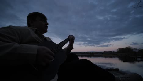 silueta de músico en negro tocando la guitarra sentado en el terraplén del muelle al atardecer