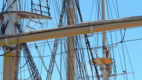 Tall-ship-rigging-gently-swaying,-backlit-against-a-clear-blue-sky,-showing-crow's-nest