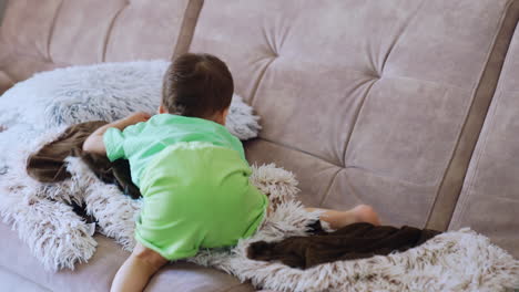 adorable toddler sits on the sofa covered with soft fluffy plaid. kid goes down on the floor and runs away.