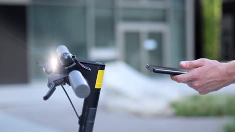 hand of young man unlock and turn on electronic scooter with smartphone application on mobile device