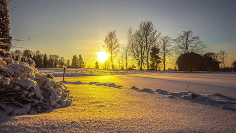 Zeitraffer-Einer-Verschneiten-Landschaft-Mit-Bäumen-Und-Einem-Holzhaus,-Auf-Das-Die-Sonne-In-Einem-Goldenen-Sonnenuntergang-Fällt