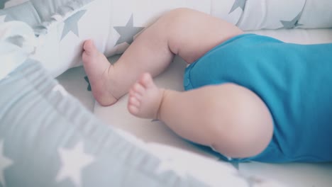 little barefoot child in blue bodysuit lies in soft cocoon