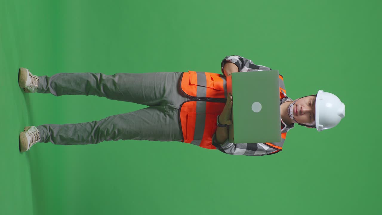 Full Body Of Asian Male Engineer With Safety Helmet Working On A Laptop While Standing In The Green Screen Background Studio