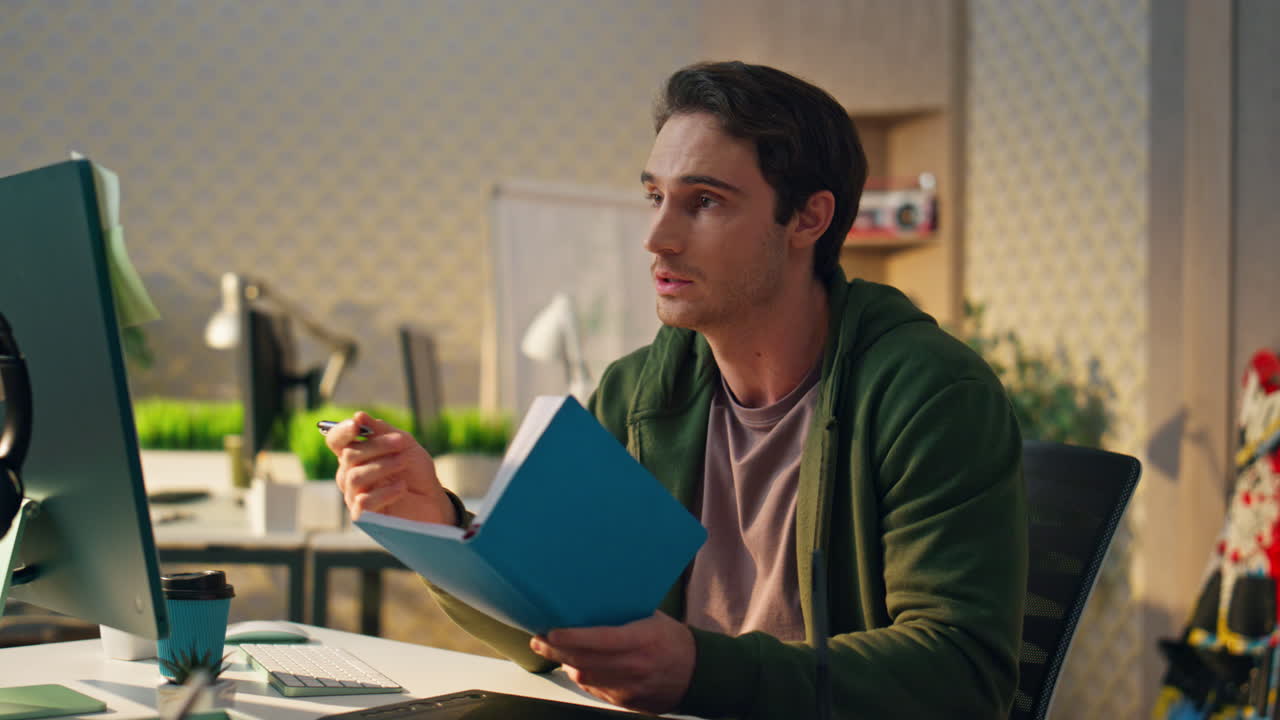 un tipo de startup leyendo un cuaderno haciendo una llamada de video en la oficina. un hombre tomando notas.