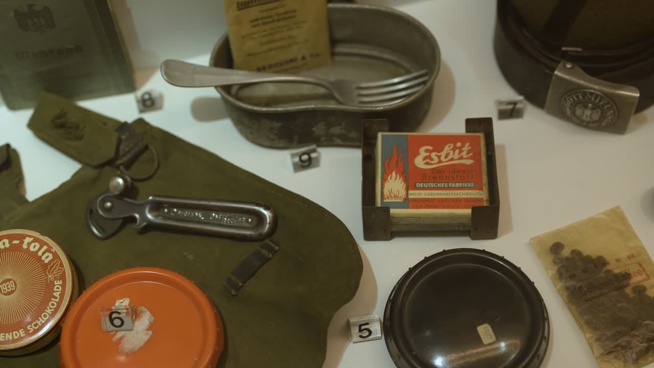 Close-up tracking shot of German WWII field rations, utensils, and gear under soft museum lighting