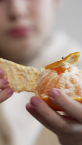 teenager's hands in focus peeling the fruit. unrecognized boy holding tangerine and taking off its peel slowly. close up. blurred backdrop. vertical video