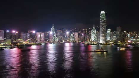the vibrant skyline of hong kong is illuminated at night, with skyscrapers and boats creating a picturesque view. bright lights reflect on the water, showcasing the city's energy.