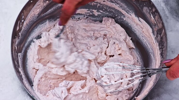 Person mixing ice cream base with a whisk, preparing a homemade frozen dessert