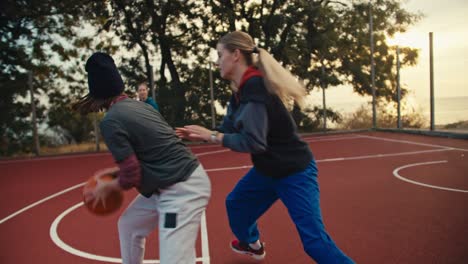 un trío de chicas rubias juegan al baloncesto con un baloncesto naranja en la cancha de baloncesto roja y una de ellas lanza la pelota en el aro de baloncestro durante su entrenamiento matutino