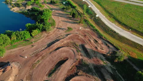 beautiful aerial of motorcross rider driving off road on dirt bikes tracks next to a lake