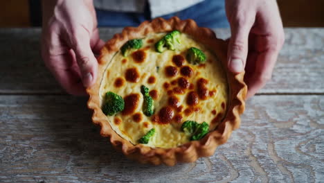 hands holding a broccoli quiche on a wooden table