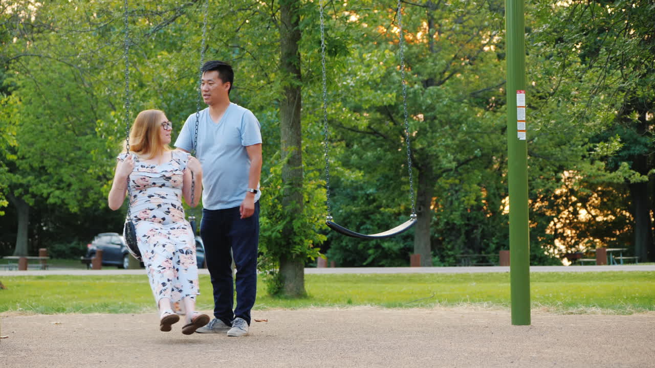 그네를 타고 공원에서 쉬고 있는 활동적인 젊은 가족 임산부와 아시아인