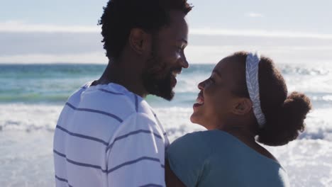 african american couple smiling, embracing and talking on the beach
