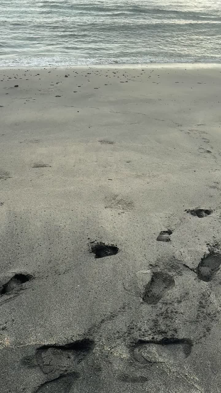 Impronte nella sabbia scura con dolci onde dell'oceano