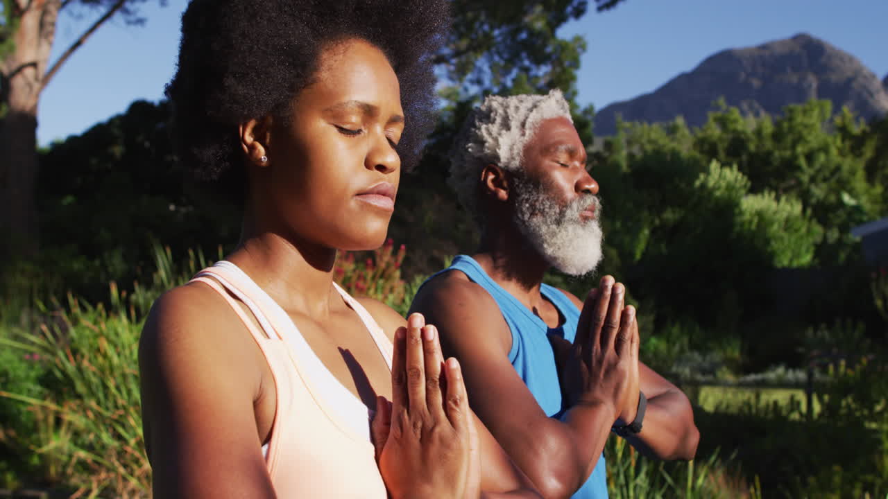 Senior african american couple practicing yoga sitting meditating in sunny garden