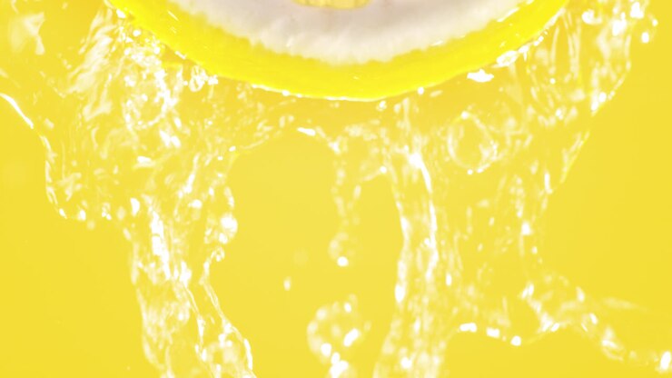 Lemon Slice Splashed With Water In Slow Motion And Macro On A Yellow Background