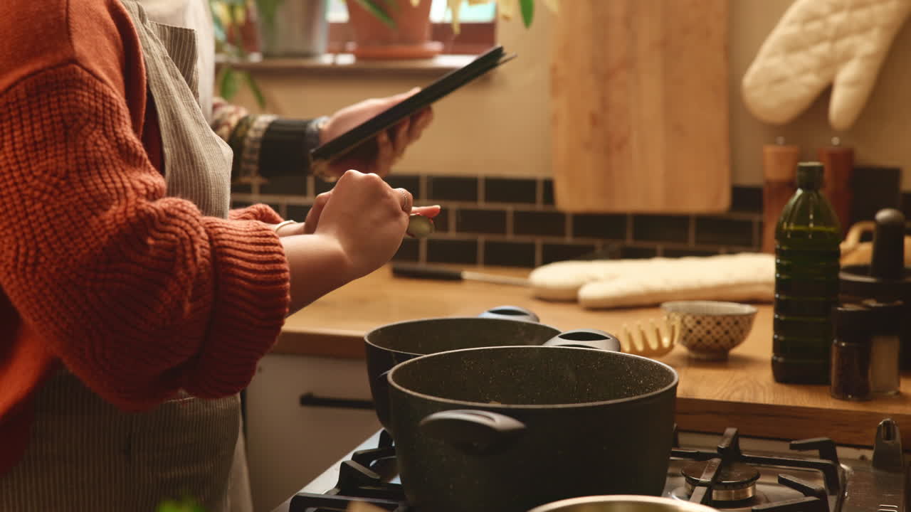 mujer siguiendo una receta en una tableta mientras cocina en la cocina