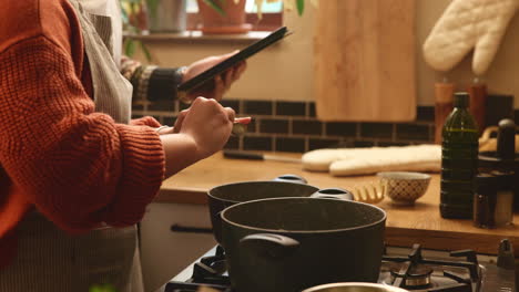 woman following a recipe on a tablet while cooking in the kitchen