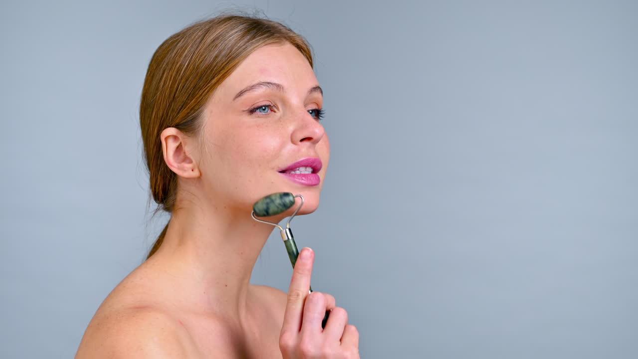 A young caucasian woman is doing facial and neck massage using a roller