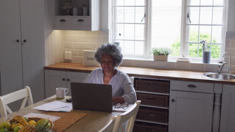 mujer afroamericana de alto nivel usando una computadora portátil y calculando las finanzas en casa
