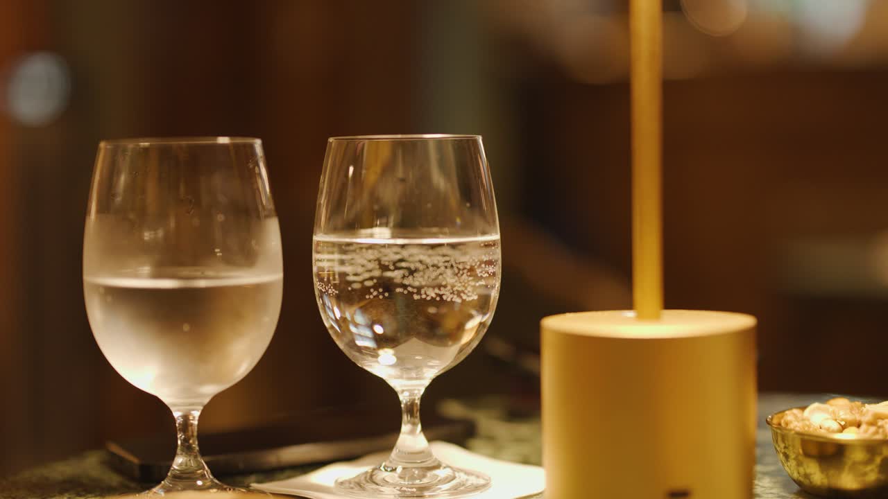 Two water glasses and candle on bar table, shallow focus, warm lighting, subtle camera movement
