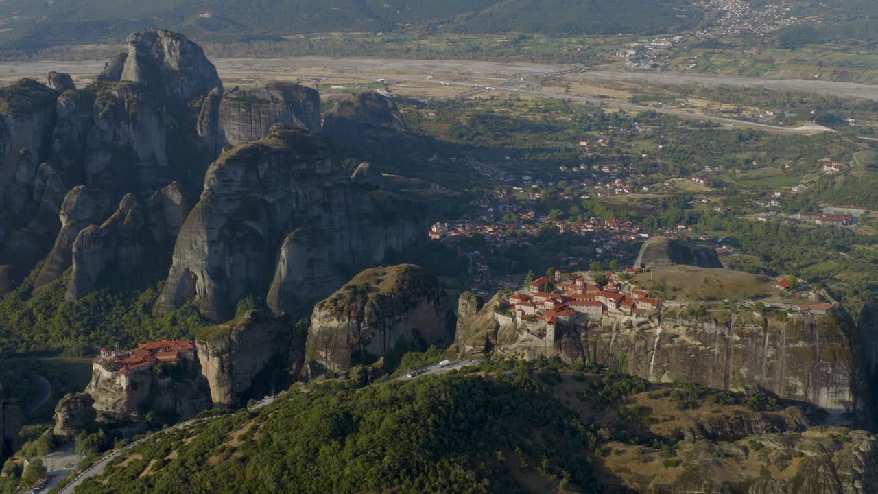 Cinematic aerial view of Meteora monastery in Greece perched on towering cliffs, dramatic rock formations and lush green valley create a breathtaking historic scene