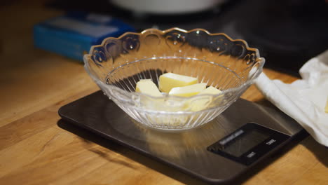 Hand-slices-butter-into-dish-on-scale-to-measure-weight,-close-up