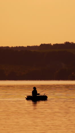 silhouette of fisherman in a boat on the natural rural evening background. beautiful sunset on the river and a man in a rowboat with fishing rods outdoors. vertical video