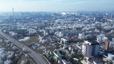 Vista-Aérea-De-Los-Automóviles-Que-Circulan-Por-La-Carretera-A-Lo-Largo-De-Los-Edificios-Con-árboles-Cubiertos-De-Hielo-En-Invierno-En-La-Ciudad-De-Galati,-Rumania