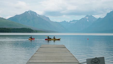 3-köpfige-Familie-Paddelkajaks-Auf-Dem-See-Im-Gletscher-Nationalpark-In-Zeitlupe-Mit-Wunderschöner-Bergkulisse-Und-Bootssteg-Im-Vordergrund