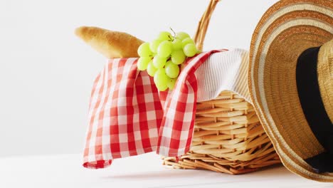 picnic basket with checkered blanket, grapes, baguette and hat on white background with copy space