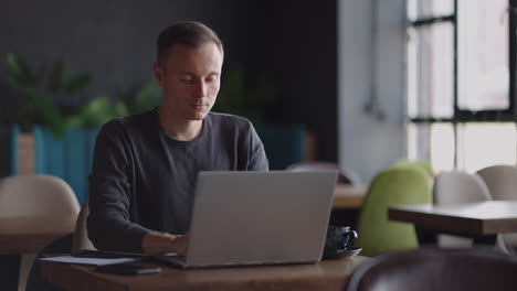 Hübscher-Freiberuflicher-Geschäftsmann-Mit-Brille,-Der-Fleißig-Am-Laptop-Im-Café-Arbeitet.-Mann-Tippt-Auf-Der-Tastatur-Und-Sucht-Im-Internet-Im-Café-Nach-Einem-Neuen-Job.-Geschäftskonzept