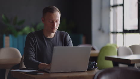 apuesto empresario independiente con gafas trabajando diligentemente en una computadora portátil en una cafetería. hombre escribiendo en el teclado y buscando un nuevo trabajo en internet en una cafetería. concepto de negocio