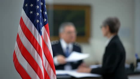 american flag in foreground with blurred official meeting and document exchange