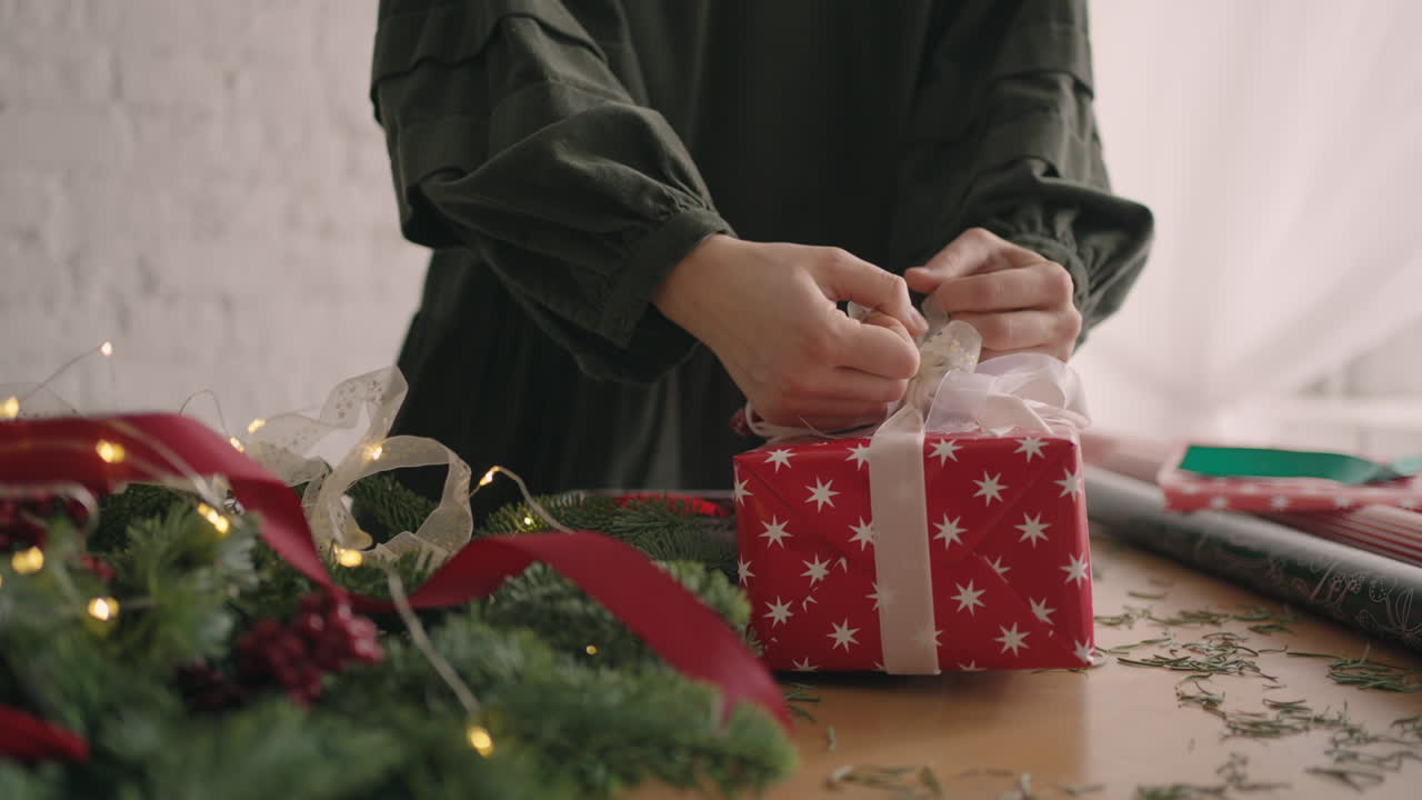 mujer envolviendo regalos de navidad. mujer atando la cinta en el regalo de navidad