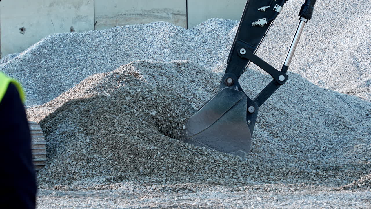 Excavator scooping gravel in a construction site, work in progress
