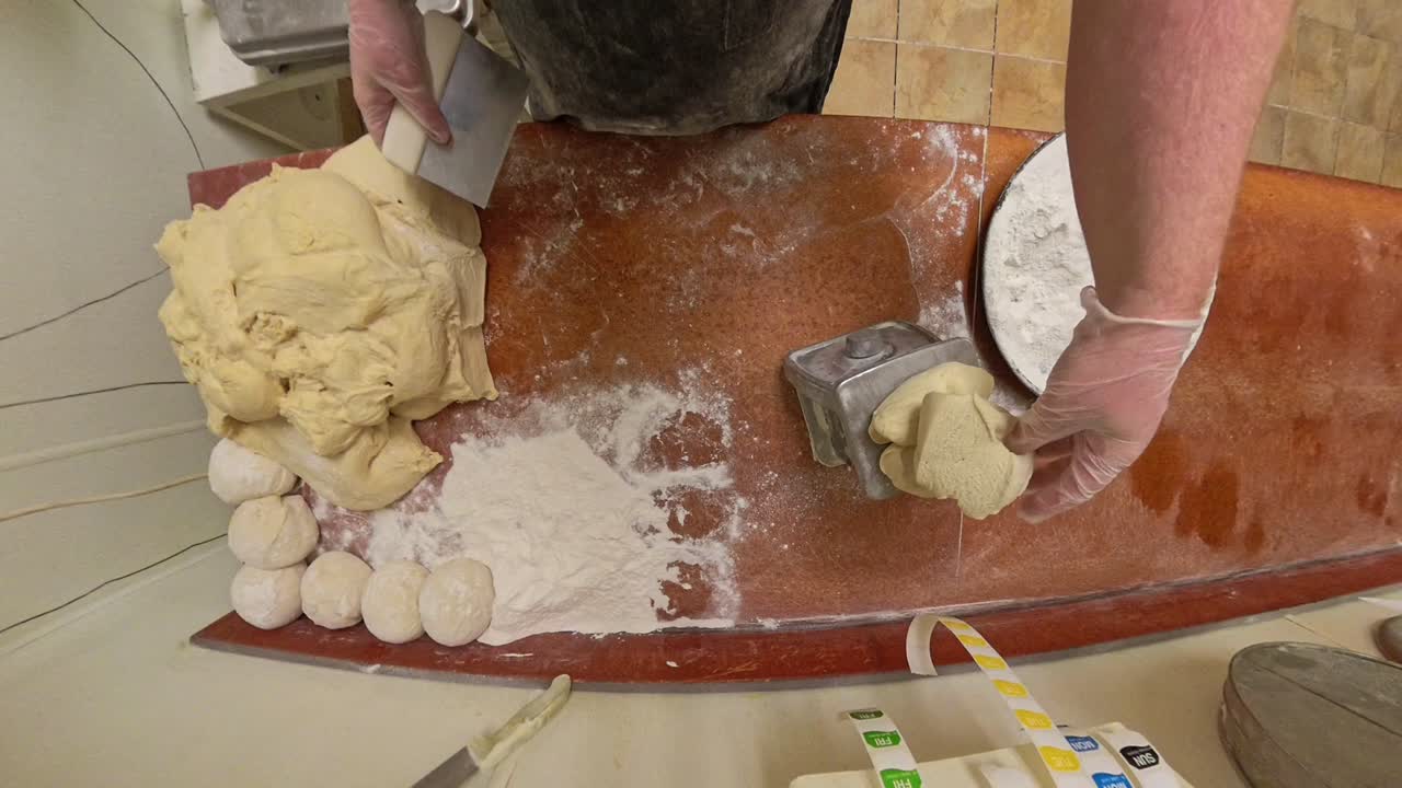 Top down of worker cutting and weighing raw dough.