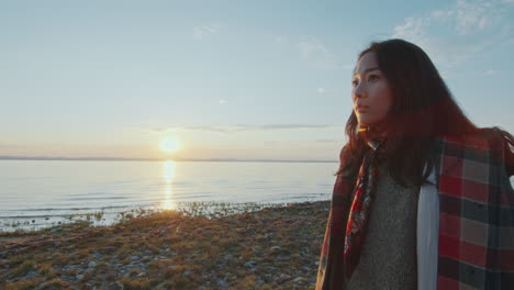 thoughtful woman standing by lakeside at sunset and gazing into distance