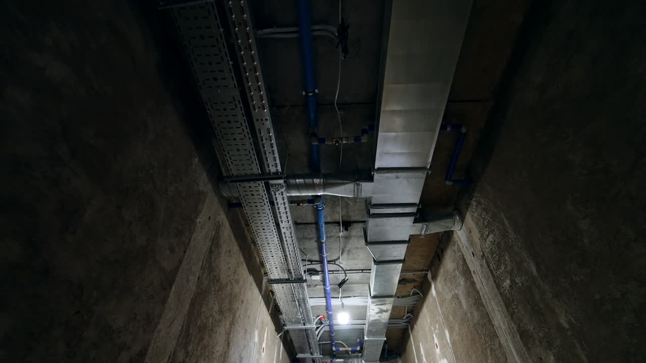 Light and ventilation communications on the ceiling of the long corridor. Low angle view. Construction site interior.