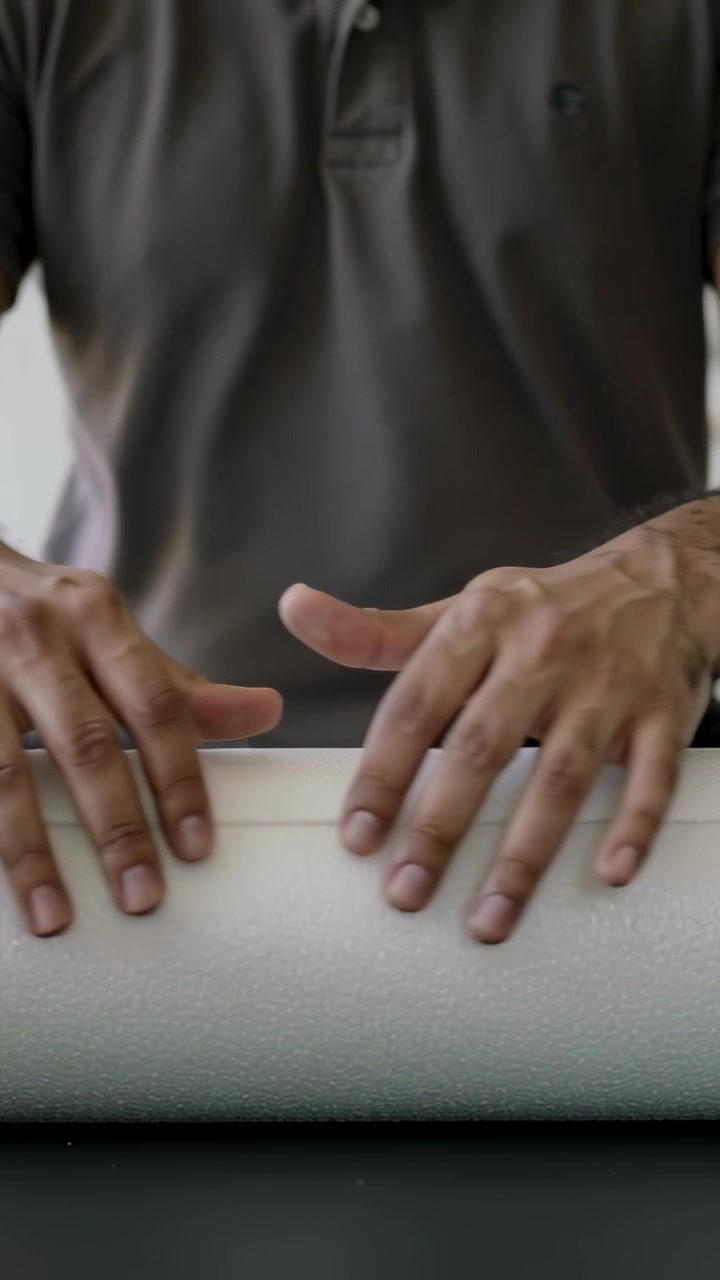 Video verticale: posizionando le mani, un uomo con polo grigia liscia un tubo di schiuma su un tavolo basso, allineando la giuntura