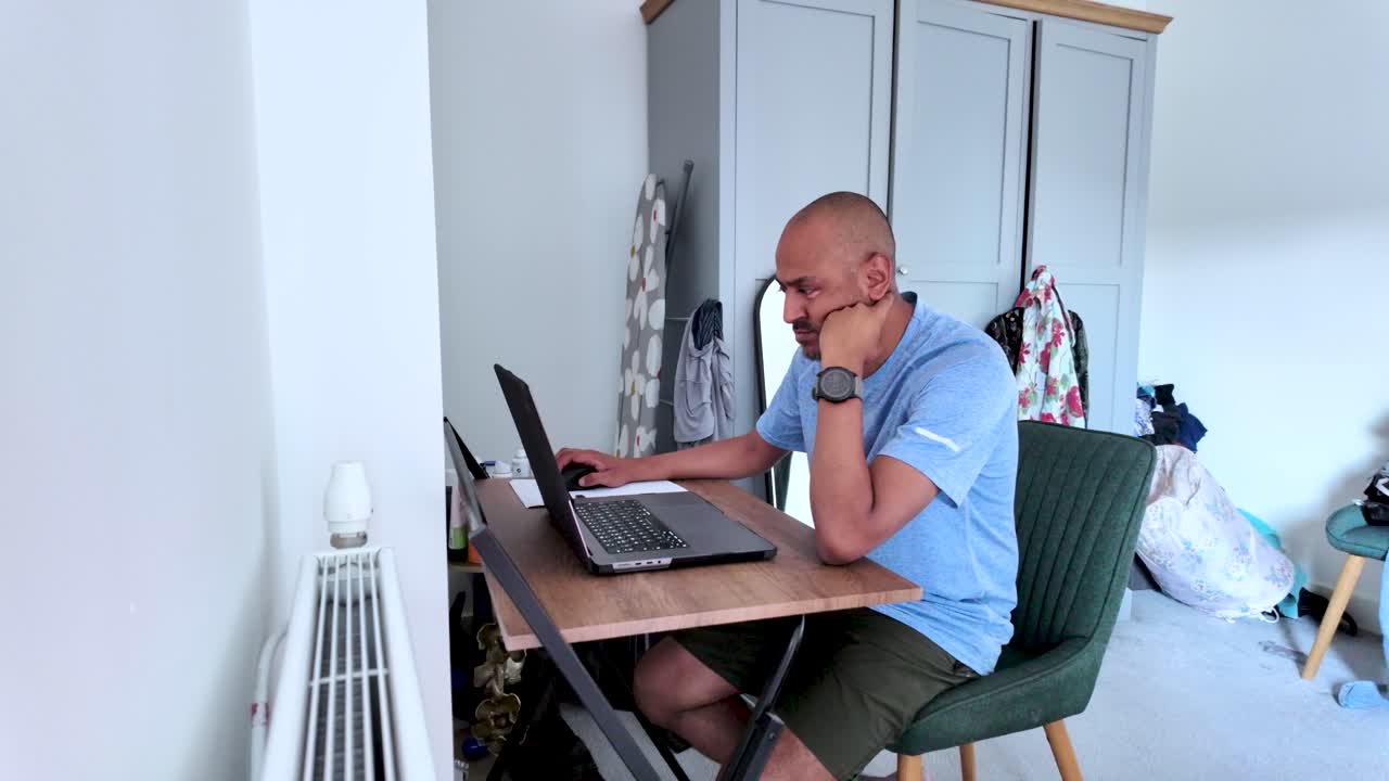 South asian man working from home in his bedroom using laptop computer