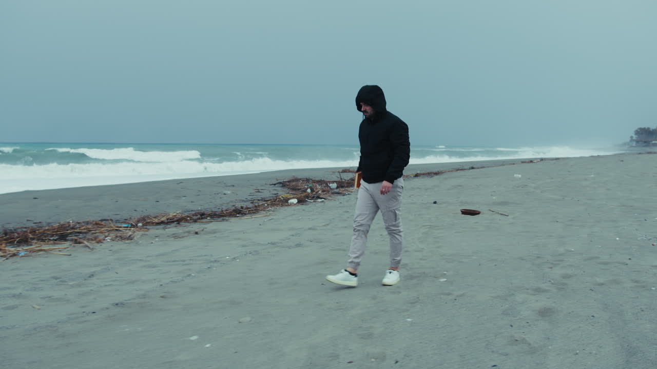 Lonely Man Walking On The Sand With A Book In Hand During The Sad Winter